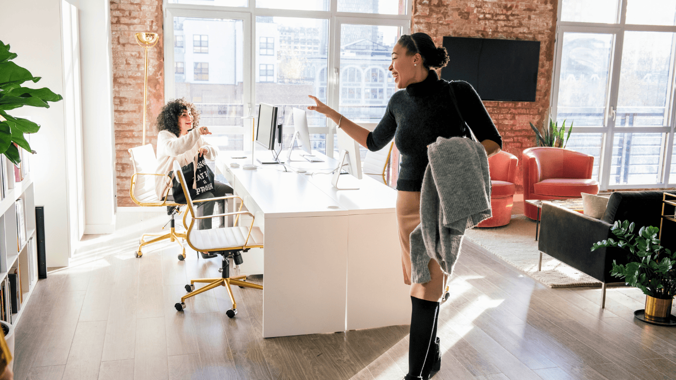 A woman waving goodbye to another woman staying late at the office.